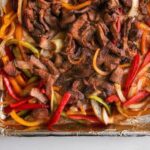 Whole30 sheet pan steak fajitas with peppers and lime on a foil tray.