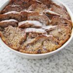 Hot cross bun pudding fresh from the oven, dusted with icing sugar on a white kitchen counter.