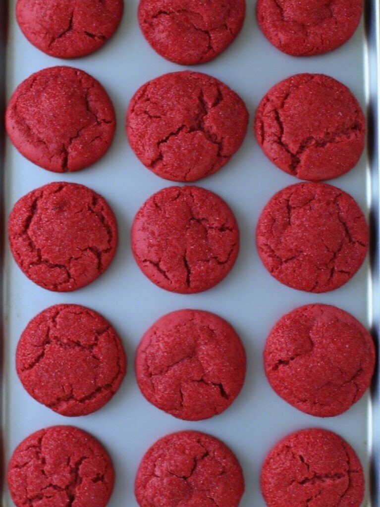 Freshly baked strawberry sugar cookies on a baking tray, with golden edges and sparkling sugar, just out of the oven, placed on a dark marble countertop.