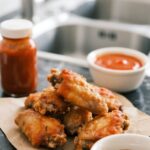 Golden crispy Whole30 chicken wings on parchment paper with sauces and fresh parsley
