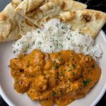 A plate of butter chicken with naan and rice, garnished with parsley, served in a rustic bowl.
